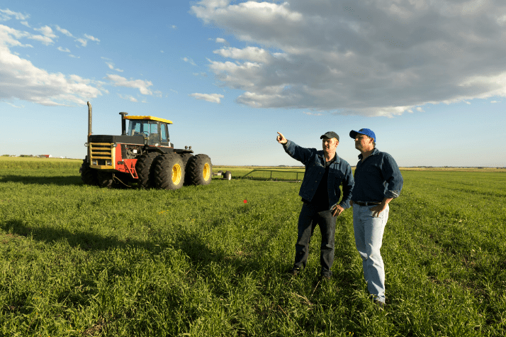 deux hommes qui discutent dans un champs avec un tracteur en fond