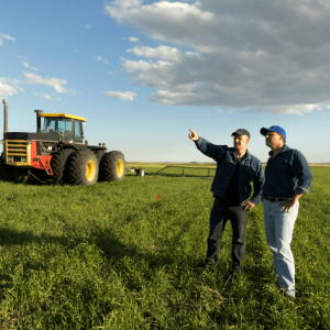 deux hommes qui discutent dans un champs avec un tracteur en fond